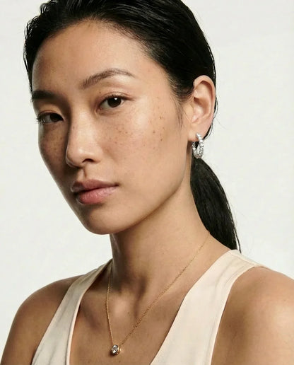 Woman wearing earrings and a necklace against a plain background