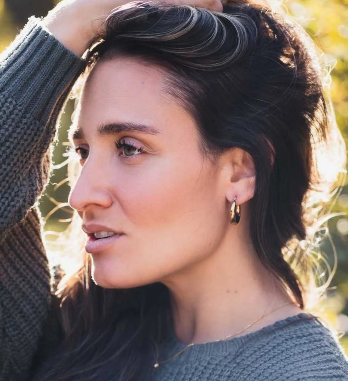 Woman with styled hair outdoors, wearing a gray sweater