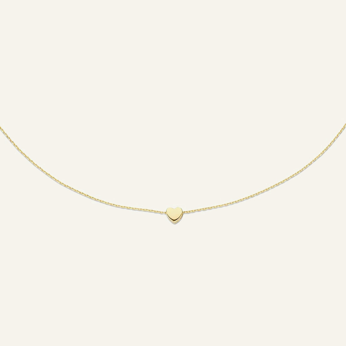 Jackie Amsterdam Plain Heart necklace in 14K yellow gold on pale beige background
