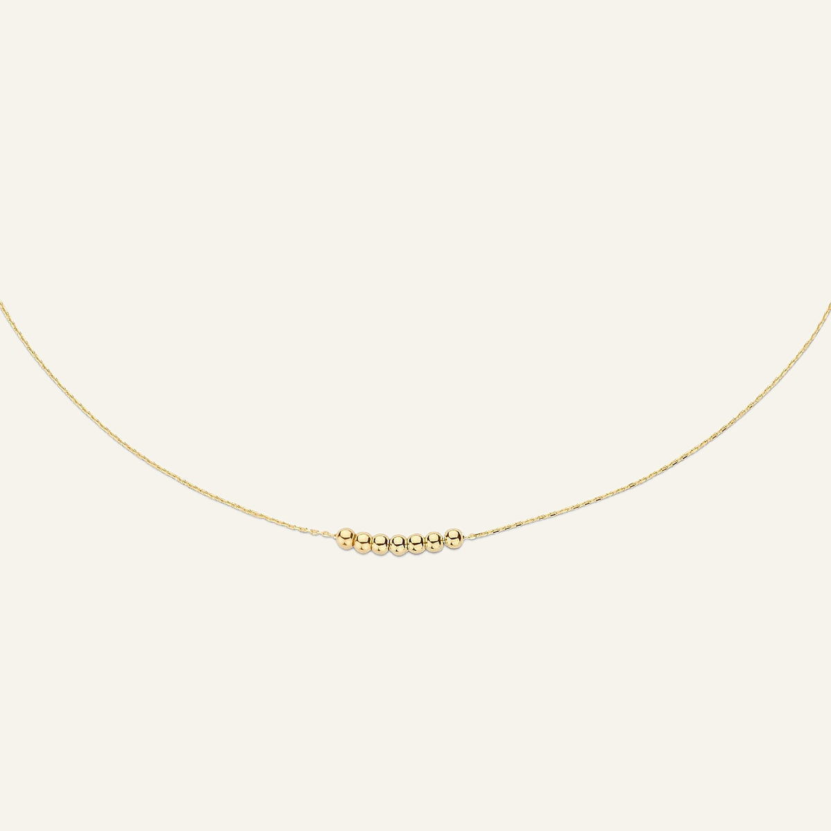 Jackie Amsterdam Mini Dots necklace in 14K yellow gold on pale beige background