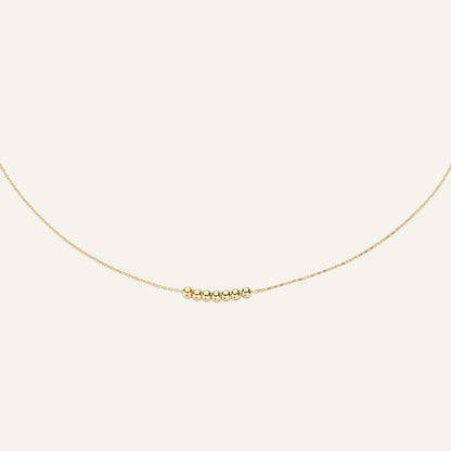 Jackie Amsterdam Mini Dots necklace in 14K yellow gold on pale beige background