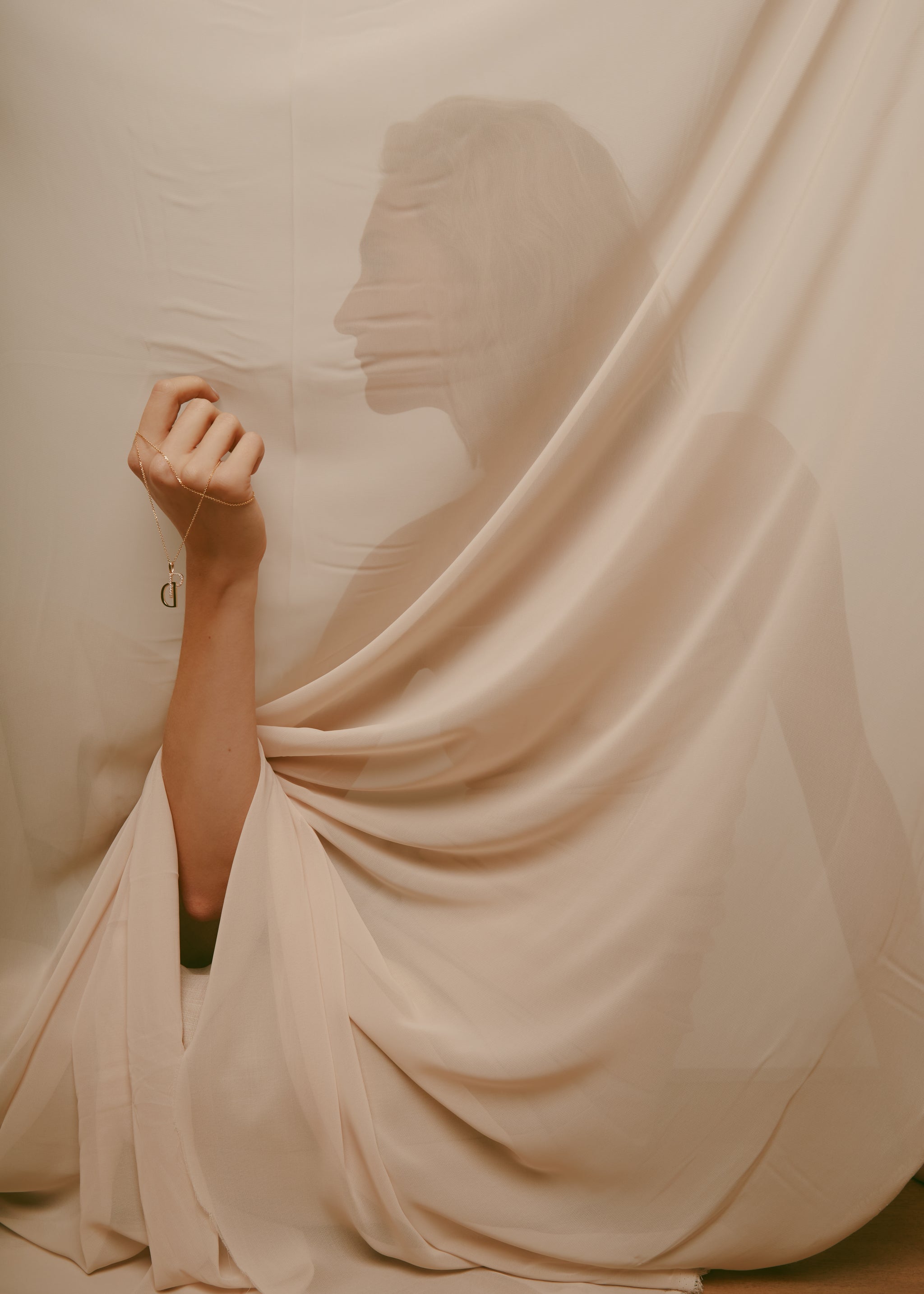 Person partially obscured by draped fabric with a soft, warm color palette.