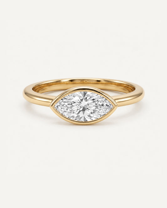 Marquise diamond bezel engagement ring in yellow gold on warm neutral background